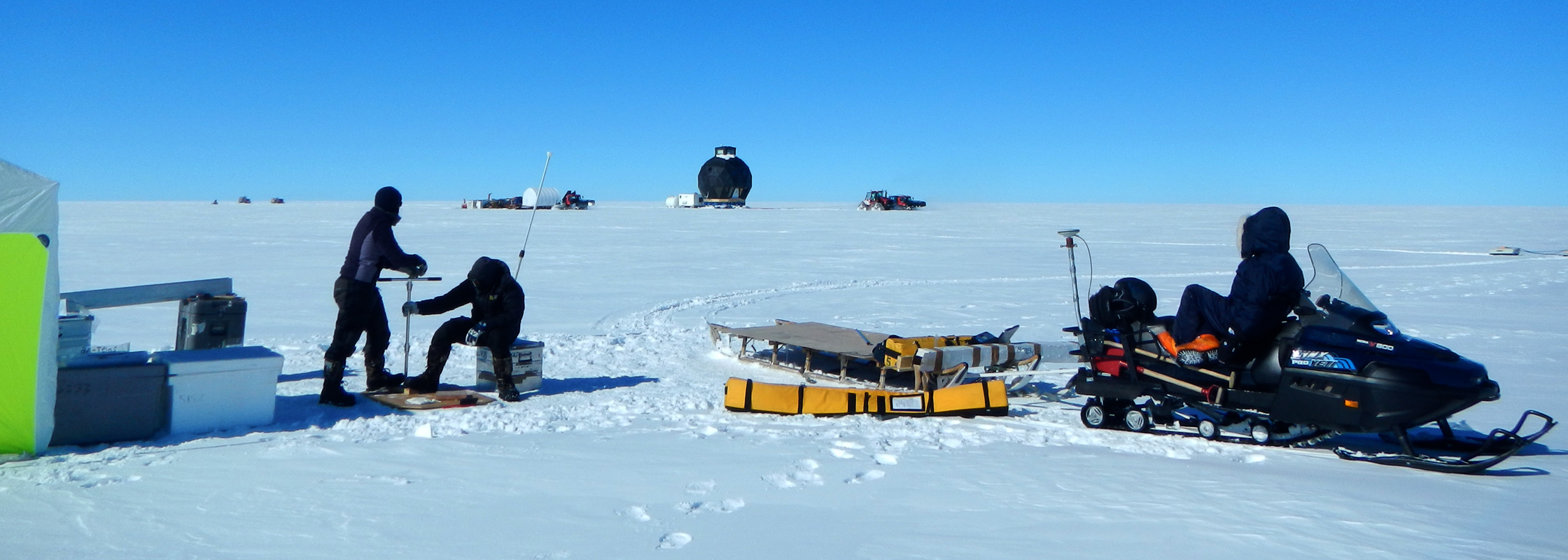 Helle and Paul are taking snow samples, while Anna is watching the traverse train go by. To the right the snowmobile with radar equipment is seen.